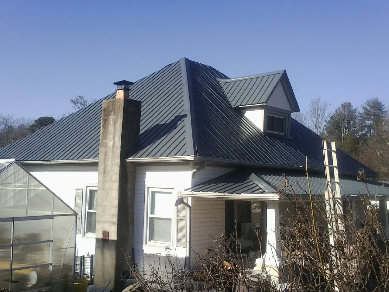 Dark blue standing seam metal roof on a white farmhouse with dormer — Slate & Tile Roof Repair by Roofing Brothers in Eatonville