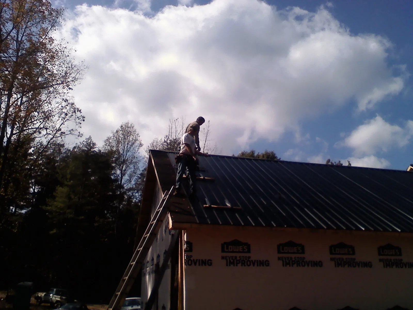 Roofer fastening dark metal panels high against a cloudy sky, from a Roof Inspection job in Eatonville