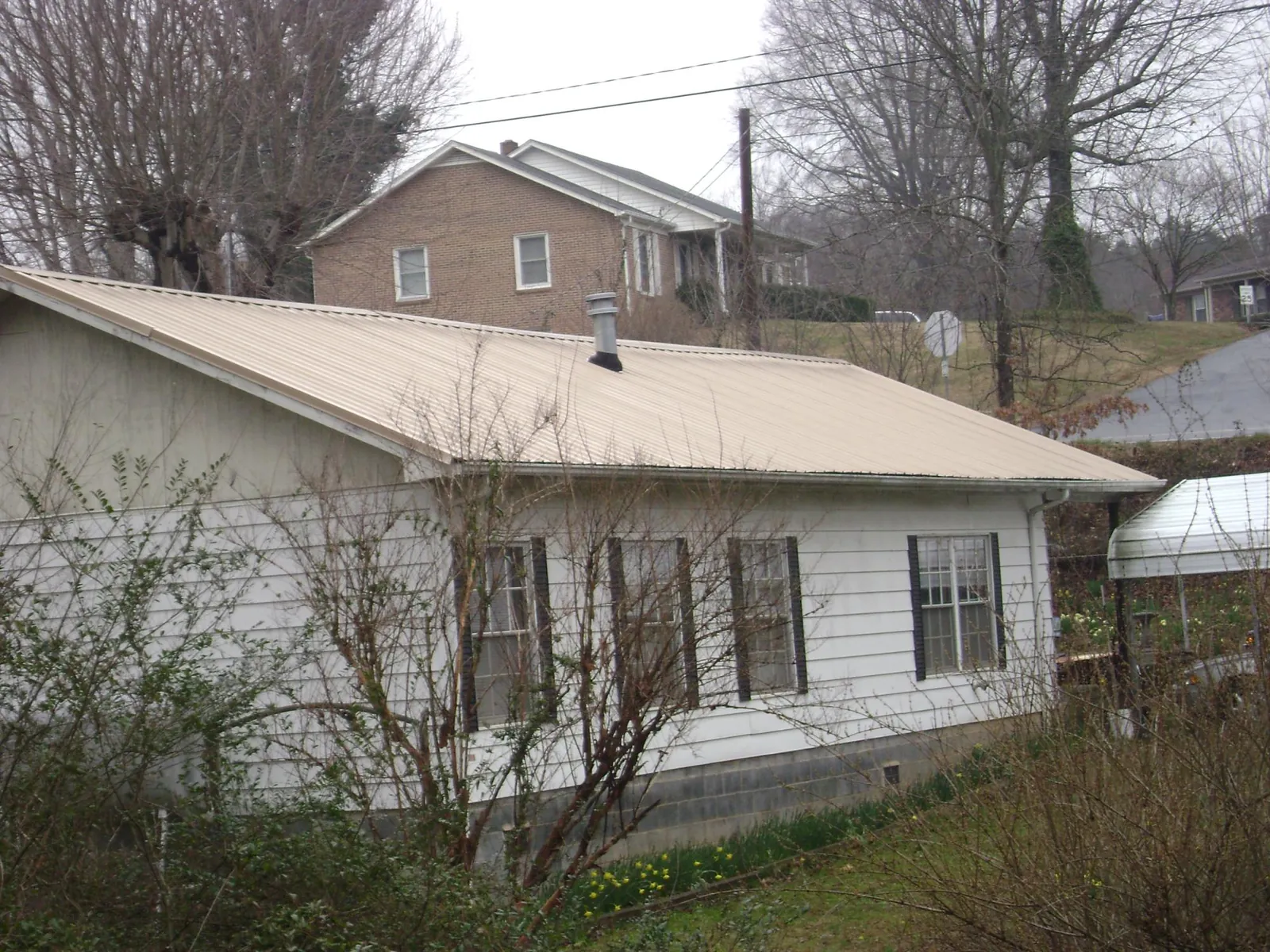Tan metal roof on a white sided house set into a hillside — Commercial Roofing by Roofing Brothers in Eatonville